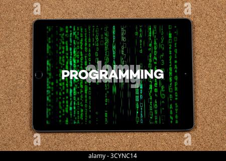 Close up to a tablet with the word programming over a green matrix code concept with a cork background Stock Photo