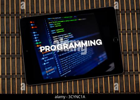 Close up to a tablet with the word programming over a writing code concept and a wooden background Stock Photo