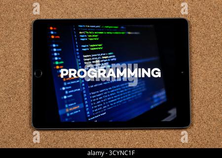 Close up to a tablet with the word programming over a writing code concept and a cork background Stock Photo