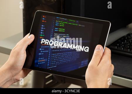 Close up to a male hands holding a tablet with the word programming over a writing code concept Stock Photo