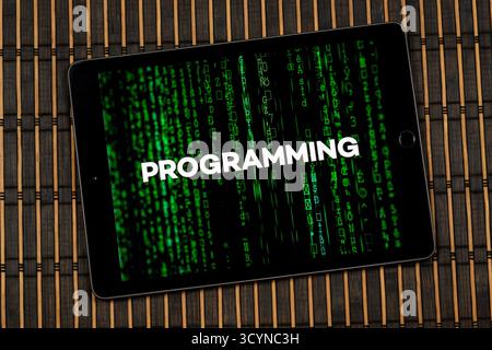 Close up to a tablet with the word programming over a green matrix code concept with a wooden background Stock Photo