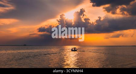 A small boat sails across the Lake Semayang under a dramatic sky as golden sunlight breaks through the clouds at sunset. Stock Photo