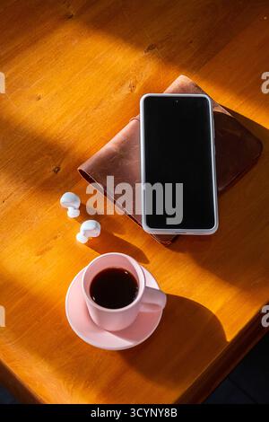 Smartphone, white earbuds and coffee cup on wooden table. Workspace flat lay with gadget and drink. Digital technology and morning concept. Stock Photo