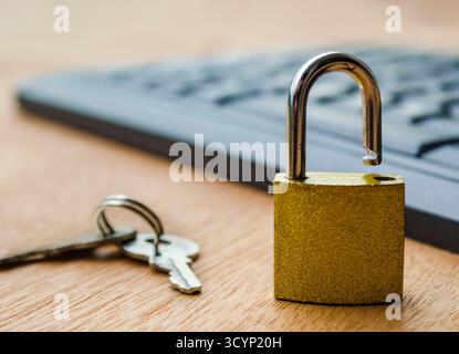 A small golden padlock standing open on a computer keyboard symbolizing cybersecurity breach and data protection risk concept Stock Photo