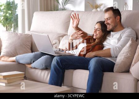 Happy couple greeting on a videocall on laptop sitting on a couch at home Stock Photo