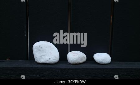 Three white stones arranged in descending size order against a dark background Stock Photo