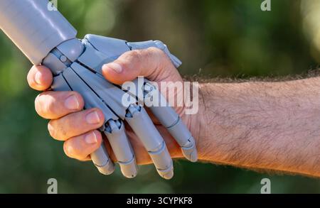 Robot and human hands. Robot and male hand handshake on green nature. Ai and human hands making handshake. Robotic hands interacting with human hand Stock Photo