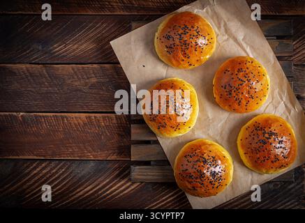 Homemade freshly baked plain golden brown soft hamburger buns topped with sesame seeds against wooden background. Homebaking Stock Photo