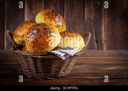 Homemade freshly baked plain golden brown soft hamburger buns topped with sesame seeds against wooden background. Homebaking Stock Photo