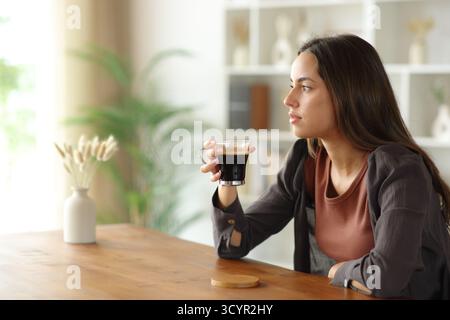 Distracted woman holding coffee cup looking away at home Stock Photo