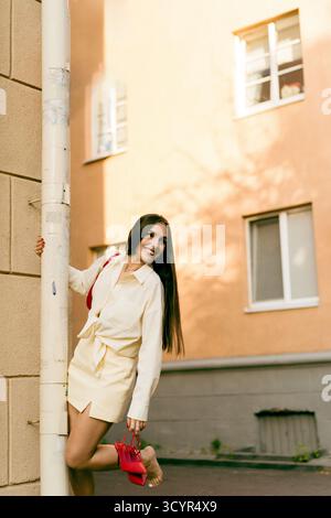 Young woman posing playfully outdoors, holding red handbag and smiling Stock Photo