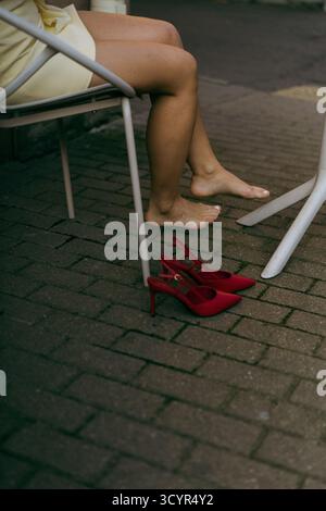 Barefoot woman relaxing on city cafe, red high heels near Stock Photo