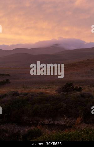 Soft pastel clouds rolling through open hill side, river, shrubs Stock Photo