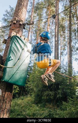Boy swinging on safety line in forest park, helmet and harness Stock Photo