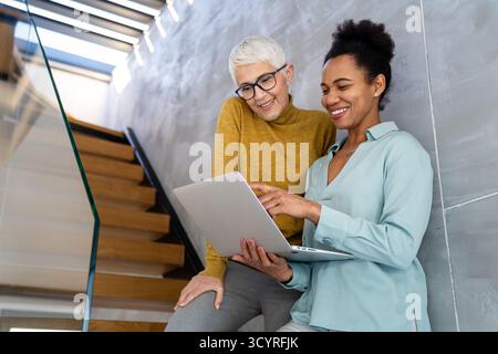 Mentorship and diversity in a modern office as colleagues share a laptop for team collaboration Stock Photo