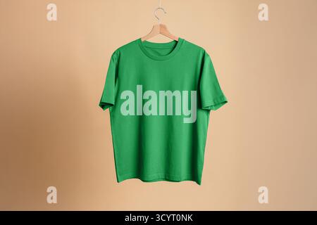 Bright green short sleeve t-shirt on wooden hanger, beige background. Mockup template for casual apparel. Clean and minimalist presentation. Stock Photo
