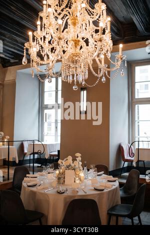 Elegant dining room with a round table set for a formal dinner under a large crystal chandelier. Stock Photo