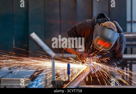 22.07.2025, Germany, , - Themed photo: metal industry. An industrial worker cuts a steel pipe with an angle grinder. 00X250722D006CAROEX.JPG [MODEL RE Stock Photo