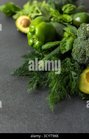 A vibrant assortment of fresh green vegetables is carefully arranged on a dark surface. This selection includes broccoli, green bell peppers, cucumber Stock Photo