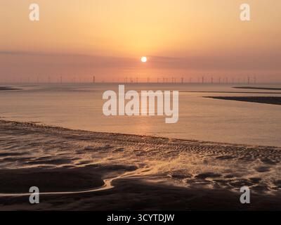 Sunset over the shoreline at low tide, New Brighton, Wirral, England. The beach displays wet sand exposed by the receding tide with the sun setting on Stock Photo
