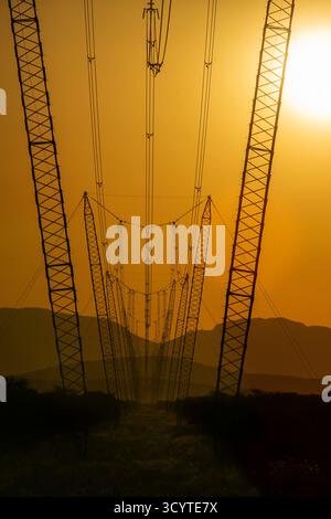 A line of power cables and pylons with the sun setting behind the Paresis Mountains in Namibia. Stock Photo