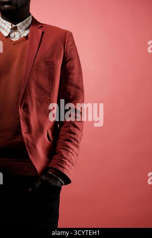 Conceptual portrait of unrecognizable Black guy in stylish outfit standing against red background with hand in pocket, half of his body seen Stock Photo