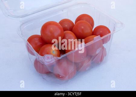 Ripe red cherry tomatoes packed in a clear plastic container on light background, healthy organic food. Stock Photo