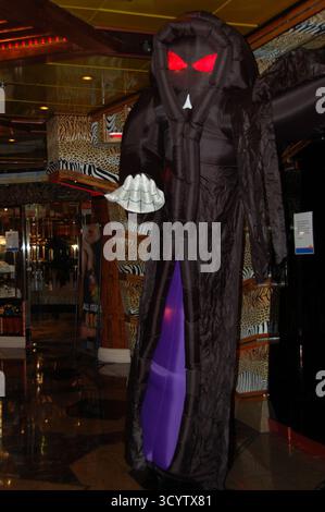 Large inflatable grim reaper Halloween decoration with glowing red eyes and a scythe inside a cruise ship hallway decorated with animal print patterns Stock Photo