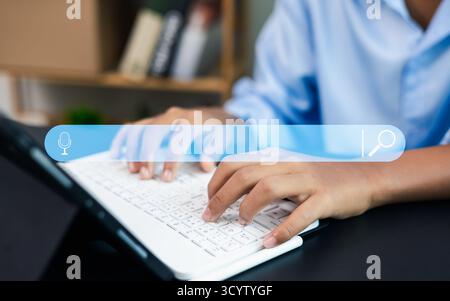 Close-up of hands typing on laptop keyboard with virtual search bar and microphone icon, representing AI assistant, voice search, and digital communic Stock Photo