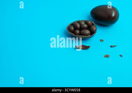 Chocolate Easter egg broken in half, candies spilling onto a bright blue background — clean food photography for festive treats and celebrations. Stock Photo