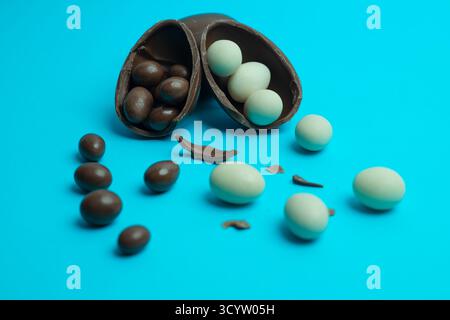 Broken chocolate Easter egg spilling chocolate-coated treats on vibrant blue; ideal for holiday, confectionery and dessert visuals. Stock Photo