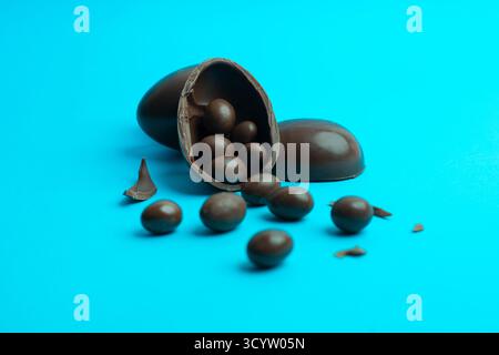 Broken chocolate Easter egg spilling chocolate-coated treats on vibrant blue; ideal for holiday, confectionery and dessert visuals. Stock Photo