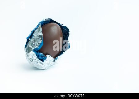 Partially unwrapped chocolate Easter egg in silver and blue foil on white; festive treat for Easter promotions, food photography, and seasonal marketi Stock Photo