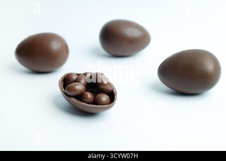 Chocolate Easter eggs on a white background, with one cracked open revealing small candies inside. A sweet treat for festive celebrations. Stock Photo