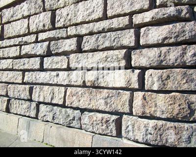 A full-frame view of a textured wall made of large, rectangular gray stone blocks, illuminated by bright sunlight. Minimalist architectural detail. Stock Photo