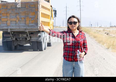 The woman is hitchhiking on the side of the road Stock Photo
