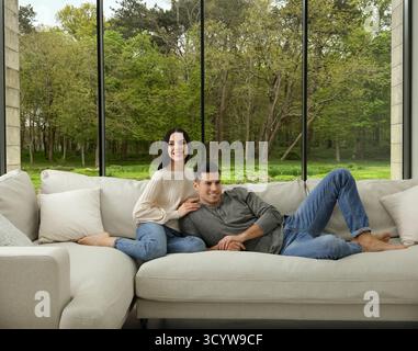 Happy couple resting on sofa near big window at home Stock Photo