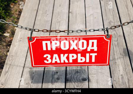 A bold red stop sign hangs on a metal chain across a weathered wooden bridge, conveying a strict barrier and restricted access in an outdoor setting. Stock Photo