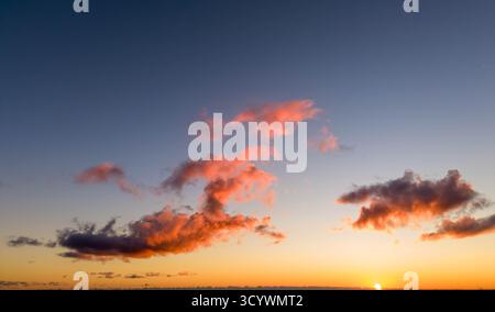 sunset scene with vibrant orange and pink clouds scattered across a clear sky as the sun dips below the horizon, casting a warm, peaceful glow Stock Photo