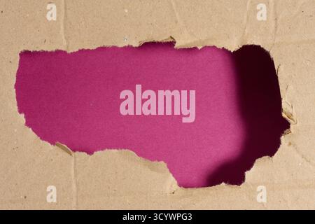 A jagged hole in a sheet of brown cardboard revealing a deep purple background. Stock Photo