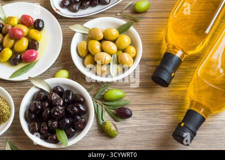 Olive varieties from Turkish Cuisine designed on white plates at a wooden surface. with two bottles of extra virgin olive oil Stock Photo