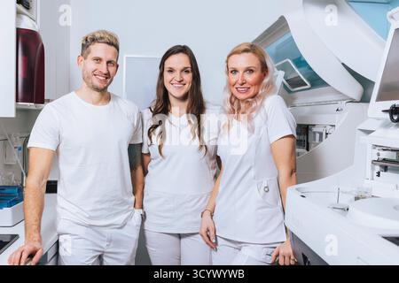 Three healthcare pros in white uniforms smile, ready to assist patients in a modern clinic. Stock Photo