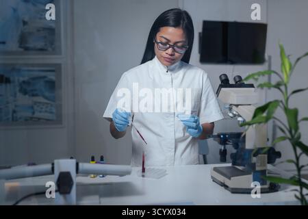 Focused female laboratory researcher observing slide through a microscope, dedicated to examining a sample. Diagnostic concept. Stock Photo