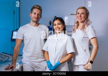 Three medical staff in bright clinic uniforms and gloves highlight teamwork and professionalism. Stock Photo