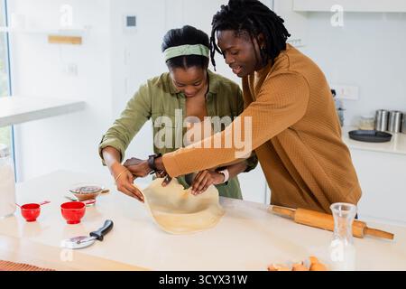 African American couple working pastry dough on kitchen island with rolling pin Stock Photo
