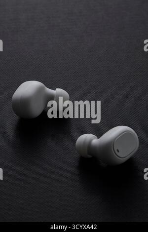 Minimalist product image showing two white wireless earbuds on dark surface representing clean design portable sound gadget and modern lifestyle techn Stock Photo