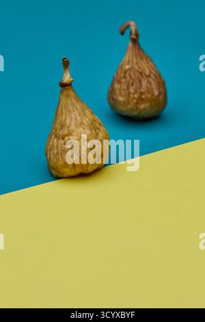 Studio image of two dried figs on split blue and yellow surface. Clean composition and natural fruit textures make perfect modern concept for organic Stock Photo