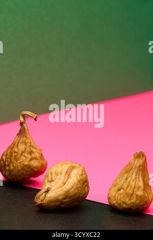Closeup of three dried figs placed on split pink and black background. Modern still life style emphasizing color contrast and organic textures of heal Stock Photo