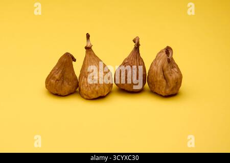 Studio composition of four dried figs arranged in a row on yellow background. Natural textures and warm tones convey healthy organic fruit and diet th Stock Photo