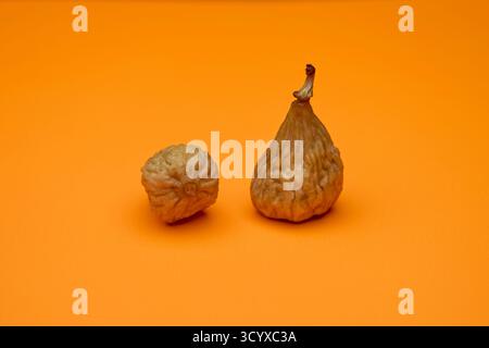 Studio shot of two dried figs on vibrant orange background. Natural textures of dried fruit highlighted by colorful design ideal for health and wellne Stock Photo